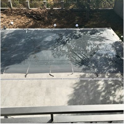 Прямоугольный бассейн с надежным темным тентом на бетонной площадке вокруг деревьев